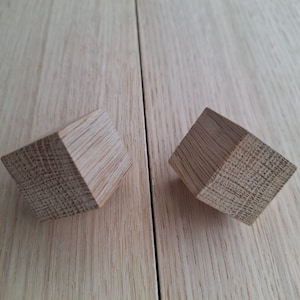 May include: Two wooden cabinet knobs with a square shape and a light brown color.