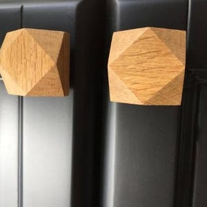 May include: Two wooden cabinet knobs with a geometric design. The knobs are light brown and have a diamond shape.
