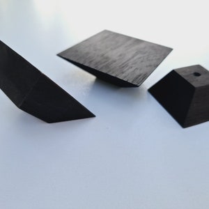 Könnte beinhalten: Drei geometrische Formen aus schwarzem Holz. Ein dreieckiges Prisma, eine quadratische Pyramide und ein rechteckiges Prisma.