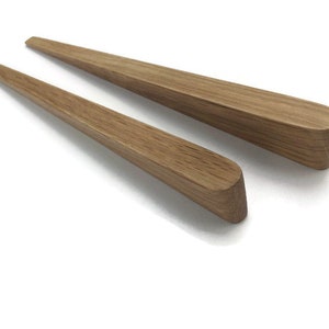 Könnte beinhalten: Zwei Holzknaufgriffe mit einem sich verjüngenden, abgerundeten Design. Die Griffe sind aus hellbraunem Holz gefertigt und haben eine natürliche Oberfläche.
