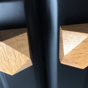 以下が含まれることがあります： 黒の表面に取付けられた、幾何学的な形をした薄い茶色の仕上げの、木製のキャビネットノブが2つあります。