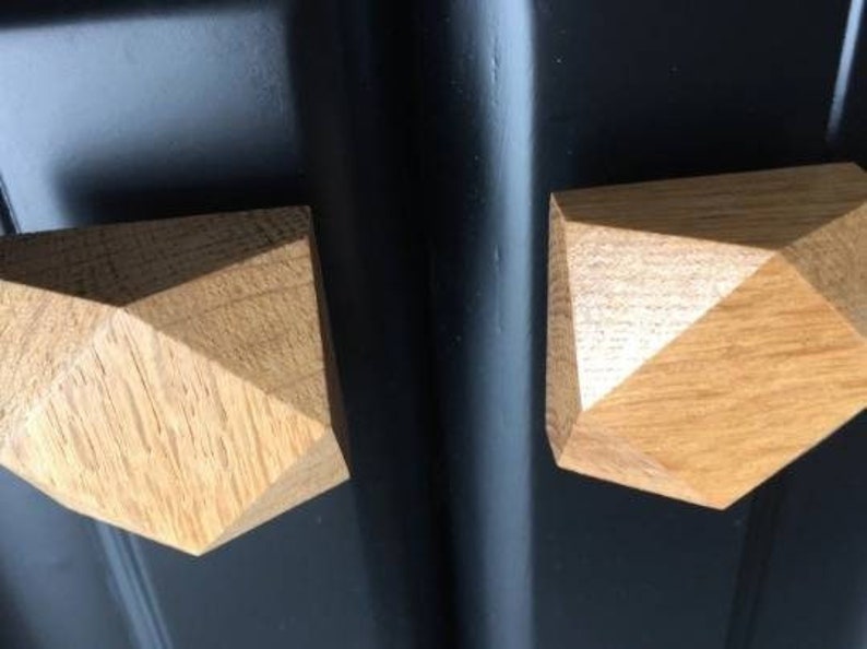 以下が含まれることがあります： 黒の表面に取付けられた、幾何学的な形をした薄い茶色の仕上げの、木製のキャビネットノブが2つあります。