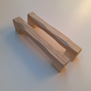 May include: Two wooden cabinet knobs with a rustic, textured finish. The knobs are light brown in colour and have a rectangular shape.