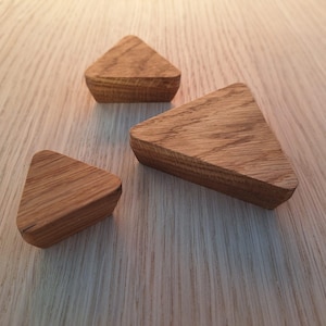 May include: Three wooden triangle shapes of varying sizes, made of light brown wood, arranged on a light wood surface.