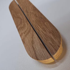 Può includere: Una maniglia per porta in legno con un design diviso, che presenta una venatura del legno naturale e un colore marrone chiaro.