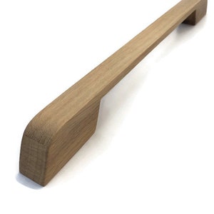 Puede incluir: Un tirador de armario de madera con forma rectangular y bordes redondeados. El tirador está hecho de madera marrón claro y tiene un diseño simple y moderno.