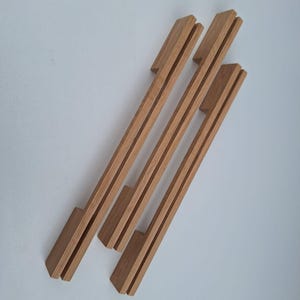 Pode incluir: Três puxadores de armário de madeira natural com forma retangular e design canelado. Os puxadores são feitos de bambu e têm uma cor castanho claro.