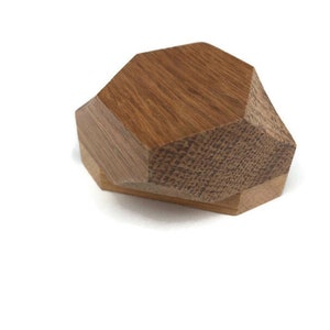 Puede incluir: Una caja geom&eacute;trica de madera con una tapa hexagonal. La caja est&aacute; hecha de dos tipos diferentes de madera, una con una veta m&aacute;s oscura y otra con una veta m&aacute;s clara.