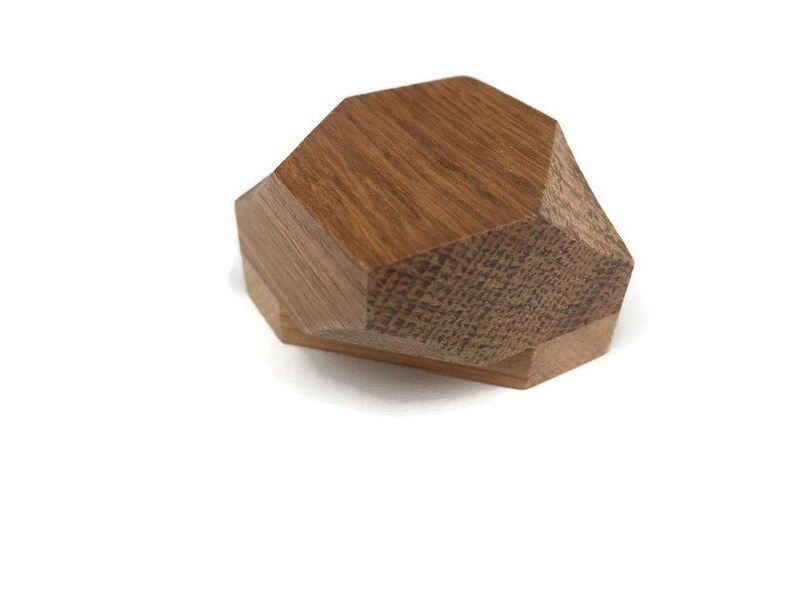 Puede incluir: Una caja geom&eacute;trica de madera con una tapa hexagonal. La caja est&aacute; hecha de dos tipos diferentes de madera, una con una veta m&aacute;s oscura y otra con una veta m&aacute;s clara.