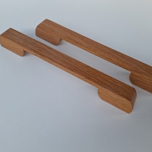 Può includere: Due maniglie per armadi in legno con un design rettangolare semplice. Le maniglie sono in legno marrone chiaro e hanno un'apertura al centro per una presa facile.