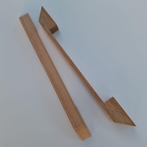 May include: Two wooden drawer pulls with a simple, modern design. The pulls are made of light brown wood and have a rectangular shape with a slight curve at the top.