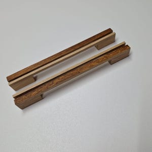 May include: Two wooden cabinet pulls with a light wood center and dark wood edges. The pulls are rectangular and have a slight curve in the center.