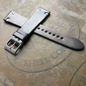 May include: Two black leather watch straps with white stitching. The straps are crossed over each other and the buckle of one strap is visible.