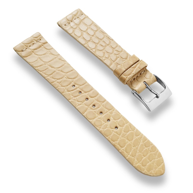 May include: A light beige alligator watch strap with a silver buckle.