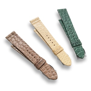 May include: Three leather watch straps in different colors: brown, beige, and green. The straps have a textured alligator pattern.
