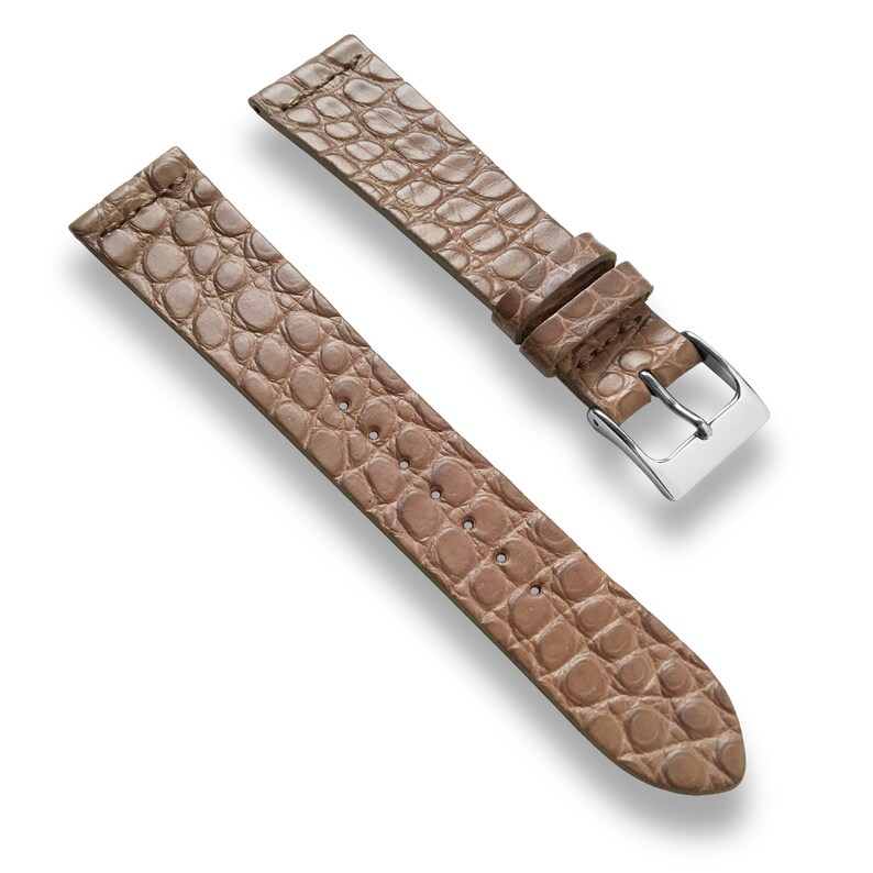 May include: A light brown leather watch strap with a crocodile pattern. The strap has a silver buckle.