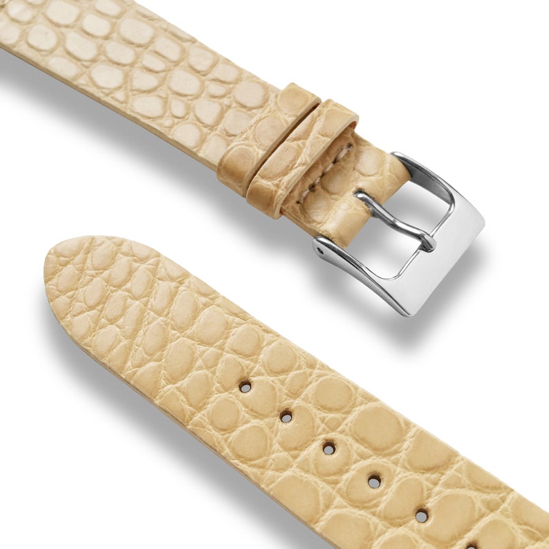 May include: A light beige alligator watch strap with a silver buckle. The strap is made of genuine leather and has a textured surface.