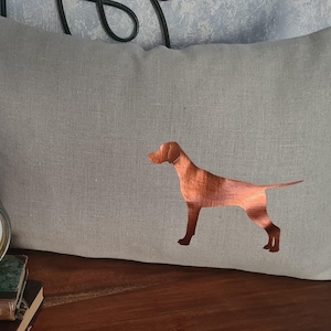 Könnte beinhalten: Ein hellbraunes Leinenkissen mit einer kupferfarbenen Silhouette eines Hundes, der auf seinen Hinterbeinen steht. Der Hund blickt nach rechts.