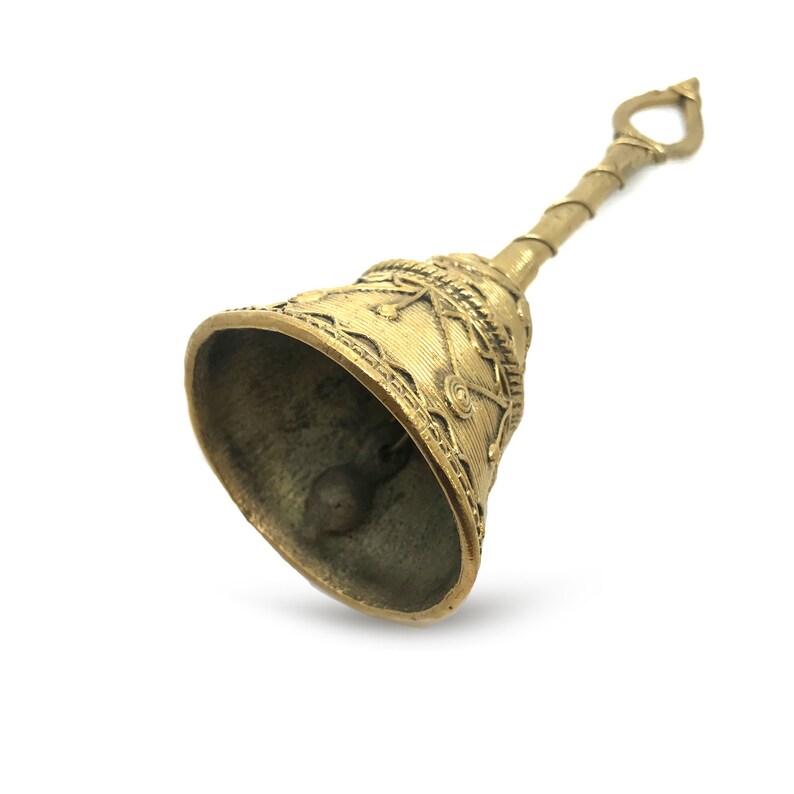 Pu&ograve; includere: Una campana di ottone con un design ornato. La campana ha un lungo manico con un anello in alto. Il corpo della campana &egrave; decorato con motivi e trame intricate. Il battaglio &egrave; visibile all'interno.