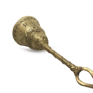 Pu&ograve; includere: Primo piano di una campana color ottone con un design ornato. La campana ha una parte superiore arrotondata con motivi intricati e un lungo manico con un'estremit&agrave; ad anello. La campana &egrave; in metallo e ha un aspetto vintage.