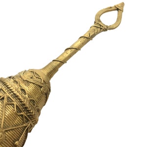 Pu&ograve; includere: Primo piano di un oggetto in metallo color oro dal design ornato. L'oggetto ha una base a forma di campana con motivi intricati e un lungo e sottile manico. Il manico presenta un design a filo avvolto e un anello all'estremit&agrave;.