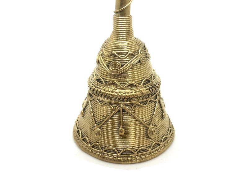 Pu&ograve; includere: Una campana color oro con intricati dettagli avvolti in filo metallico e motivi decorativi. La campana ha una base svasata e un lungo e sottile manico. Il design include forme geometriche e motivi a spirale, creando una superficie strutturata.