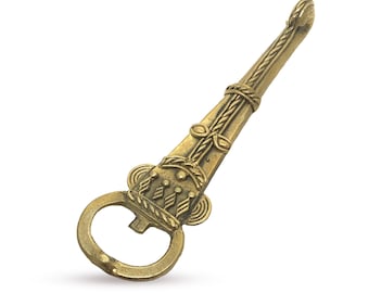 Può includere: Un apribottiglie dorato con un designo ornato. L'apribottiglie ha la forma di una lama lunga e sottile con un anello all'estremità per aprire le bottiglie.