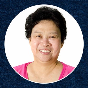 May include: A woman with short, dark hair smiles at the camera. She is wearing a pink shirt.