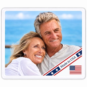 May include: A rectangular coaster featuring a photograph of a smiling couple with blonde and grey hair against a blue ocean background. A diagonal blue banner across the bottom right corner contains the text Made in USA and a small American flag.