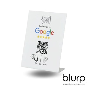 May include: White tabletop sign with a place for a logo, the text "Review us on Google" with five yellow stars, a black and white QR code, and the text "TAP OR SCAN". The sign has a white background and black text. The sign is on a white surface. The text "blurp" and "www.blurpdevices.com" are at the bottom of the sign.