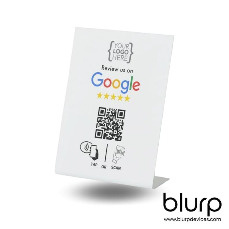 May include: White tabletop sign with a place for a logo, the text "Review us on Google" with five yellow stars, a black and white QR code, and the text "TAP OR SCAN". The sign has a white background and black text. The sign is on a white surface. The text "blurp" and "www.blurpdevices.com" are at the bottom of the sign.