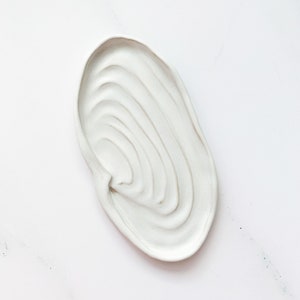 Puede incluir: Plato de cerámica blanco con forma ondulada orgánica y diseño texturizado de círculos concéntricos.