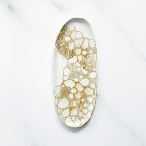 May include: An oval-shaped serving platter with a white base and a unique brown and white bubble pattern. The design covers a portion of the platter, creating an artistic contrast. The platter is ideal for serving appetizers or small dishes.