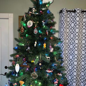 May include: A decorated Christmas tree with a snowman on top. The tree is decorated with ornaments, lights, and a variety of other decorations. The tree is in a room with a white door and a patterned curtain.