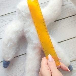 May include: A white fluffy handmade toy shaped like a person with blue feet and a yellow ruler measuring 17 inches long.