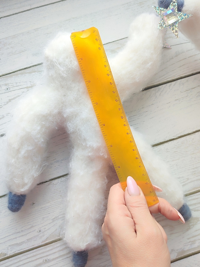 May include: A white fluffy handmade toy shaped like a person with blue feet and a yellow ruler measuring 17 inches long.