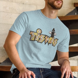 May include: A light blue t-shirt featuring a vintage-style graphic of a person holding two plates and the text "Tsssssss".