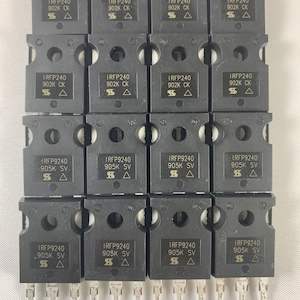 May include: A close-up view of twelve black electronic components, arranged in four rows of three. Each component has a silver label with the text "IRFP240" and either "902K CK" or "905K SV". The components have two silver leads extending from the bottom.