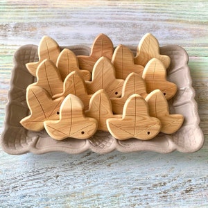 Può includere: Una collezione di sagome in legno color marrone chiaro a forma di foglia con venature del legno visibili e un piccolo foro vicino alla base di ogni pezzo, disposte su un vassoio rettangolare in ceramica beige testurizzata.