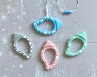 May include: Four silicone teething toys shaped like seashells in blue, gray, pink, and green with white accents. The toys are strung on a white cord with a blue bead.
