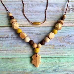 Puede incluir: Un collar de madera con cuentas marrones, amarillas y de madera natural. El collar tiene un colgante en forma de hoja.
