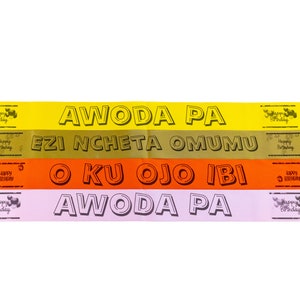 以下が含まれることがあります： 黒い文字で「AWODA PA」、「EZI NCHETA OMUMU」、「O KU OJO IBI」、「AWODA PA」と書かれた4つのカラフルな紙の横断幕。各横断幕には小さな「Happy Birthday」のグラフィックがあります。