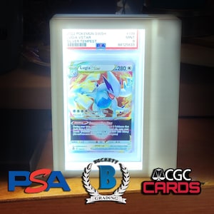 May include: A Pokémon trading card featuring Lugia VSTAR, graded and encased in a lit display. The card is from the 2022 Pokémon SWSH Silver Tempest set. The card is graded as Mint 9 by Beckett Grading Services.