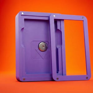 May include: A lilac rectangular case with a sliding frame, set against an orange background. The case has a circular metal element and a recessed area. The frame is open, revealing the interior.