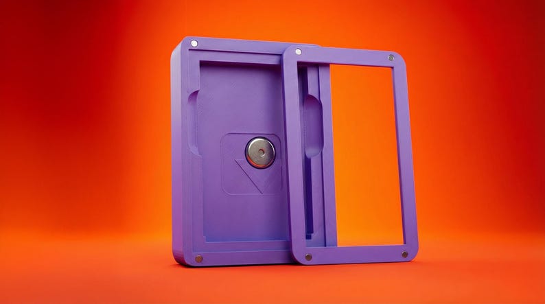 May include: A lilac rectangular case with a sliding frame, set against an orange background. The case has a circular metal element and a recessed area. The frame is open, revealing the interior.