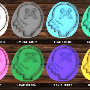 K&ouml;nnte beinhalten: Acht Ausstecher in verschiedenen Farben, jeweils in Form eines menschlichen Kopfes mit einem stilisierten Design auf der Stirn. Die Farben sind strahlend wei&szlig;, Rauchgrau, hellblau, Malibu-Blau, Posh-Pink, Blattgr&uuml;n, Psy-Lila und Goldgelb.