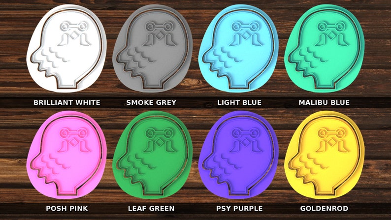 K&ouml;nnte beinhalten: Acht Ausstecher in verschiedenen Farben, jeweils in Form eines menschlichen Kopfes mit einem stilisierten Design auf der Stirn. Die Farben sind strahlend wei&szlig;, Rauchgrau, hellblau, Malibu-Blau, Posh-Pink, Blattgr&uuml;n, Psy-Lila und Goldgelb.