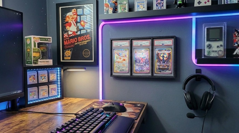 May include: A gaming setup with a wooden desk, keyboard, and mouse. A framed "Mario Bros." poster hangs on the wall, along with graded trading cards and a display case of video game cartridges. A headset and a Game Boy are also visible.