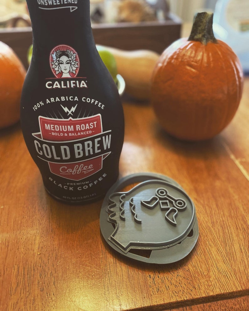 K&ouml;nnte beinhalten: Eine schwarze Flasche Califia Farms Cold Brew Coffee mit dem Text "100% Arabica Coffee" und "Medium Roast - Bold & Balanced - Cold Brew Coffee" auf dem Etikett. Die Flasche steht auf einer Holzoberfl&auml;che neben einem grauen 3D-gedruckten Objekt.