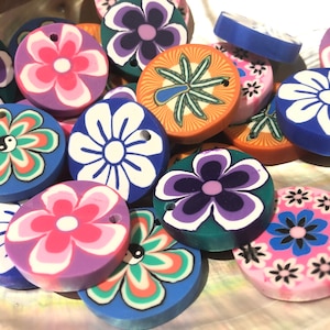 May include: Assortment of colourful round polymer clay charms with various floral and abstract designs. The charms feature a hole for hanging or attaching to jewellery or other crafts.